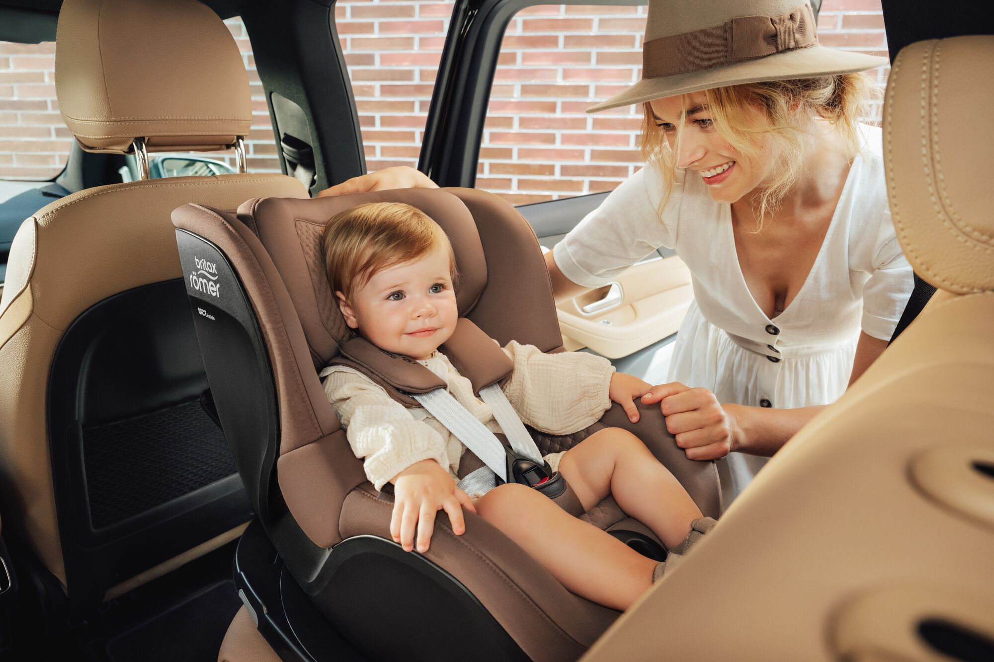 Småbarn fastspänt i en DUALFIX 5Z toddler car seat, med sin mamma stående vid sidan.